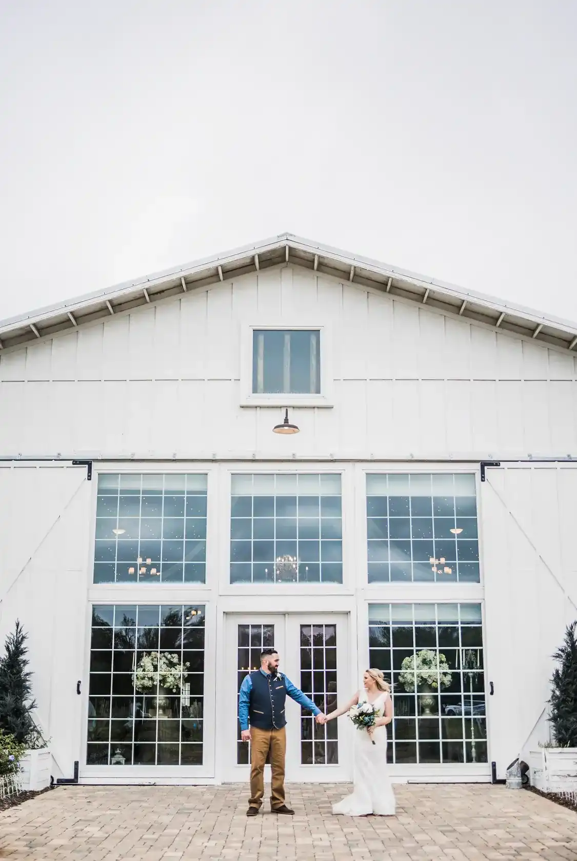 A couple holding hands in front of a white barn wedding venue