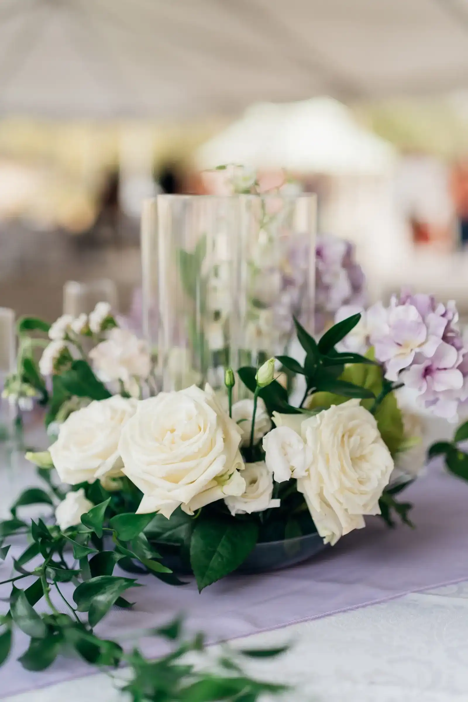 A centerpiece of white roses and lavender hydrangea on a lavender runner