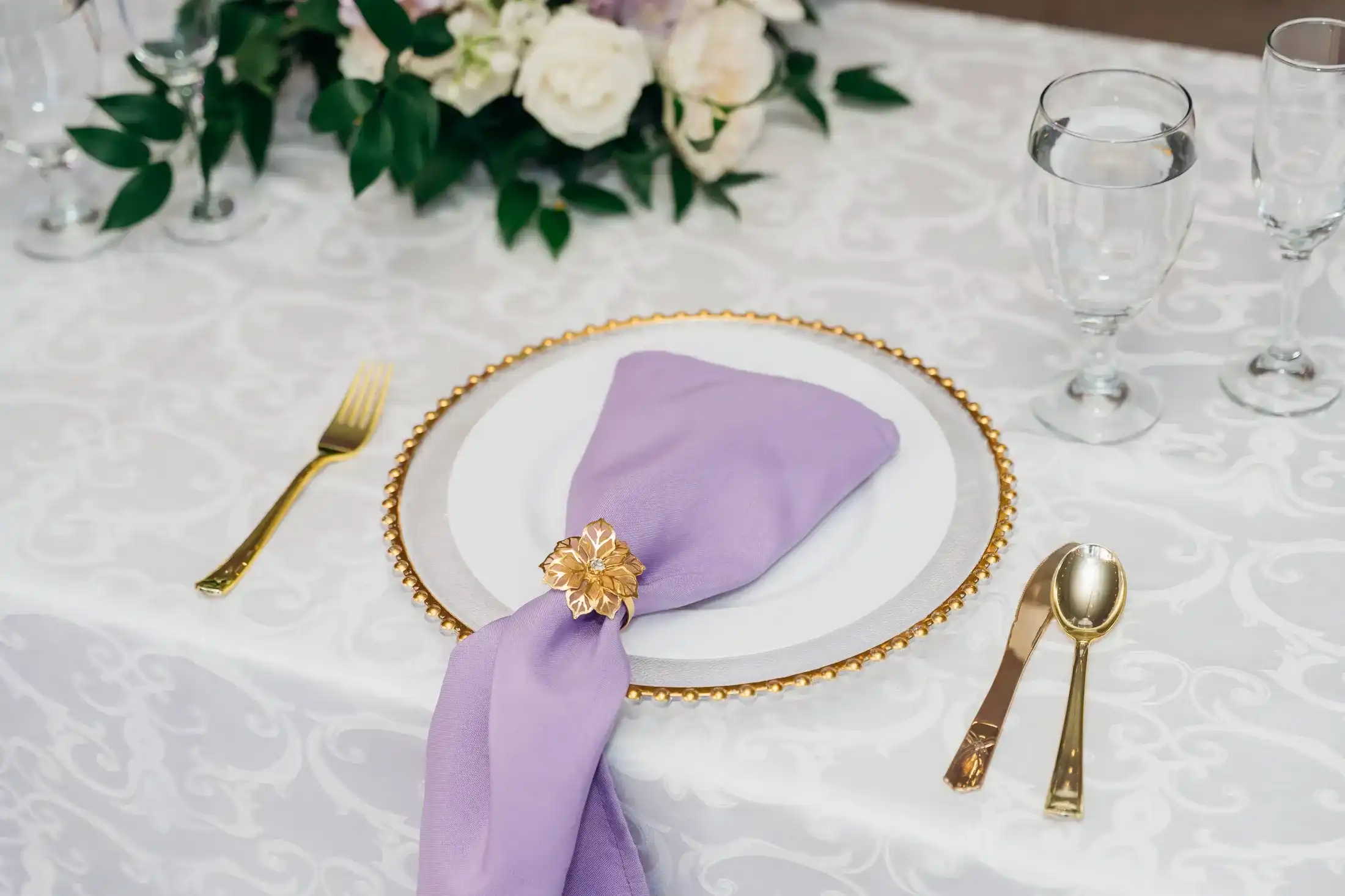 A place setting with a lavender napkin, gold charger and gold flatware