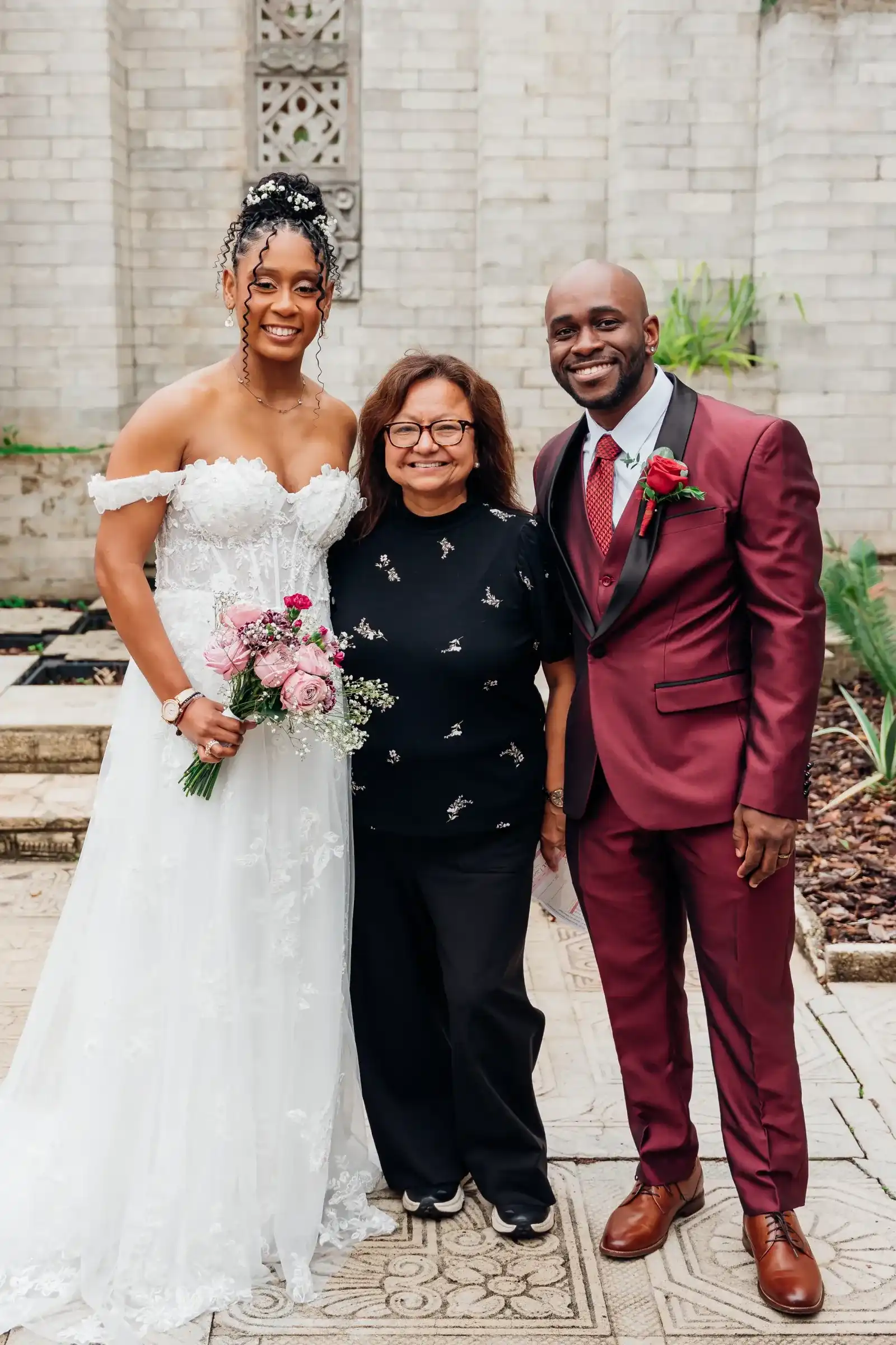 Rocío standing between a bride and groom after their ceremony in a brick courtyard