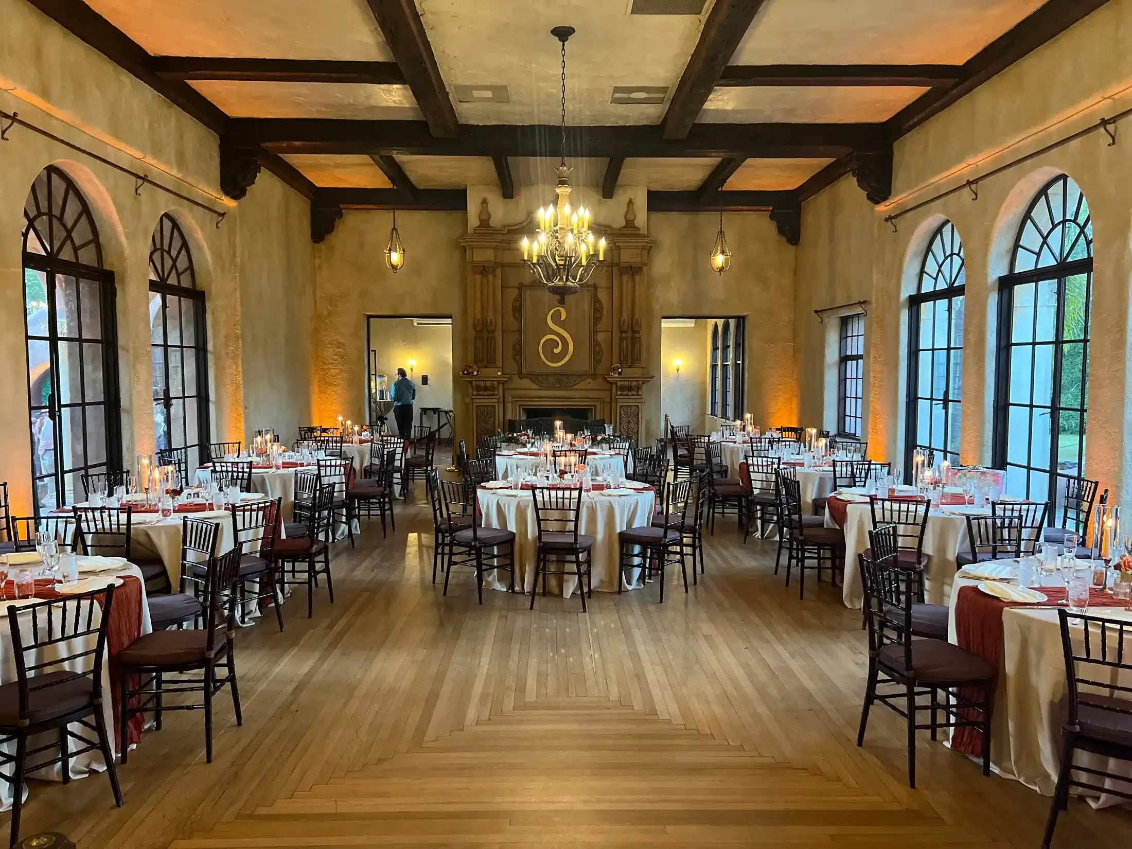 A historic ballroom set for a wedding reception with round tables, candles and a chandelier